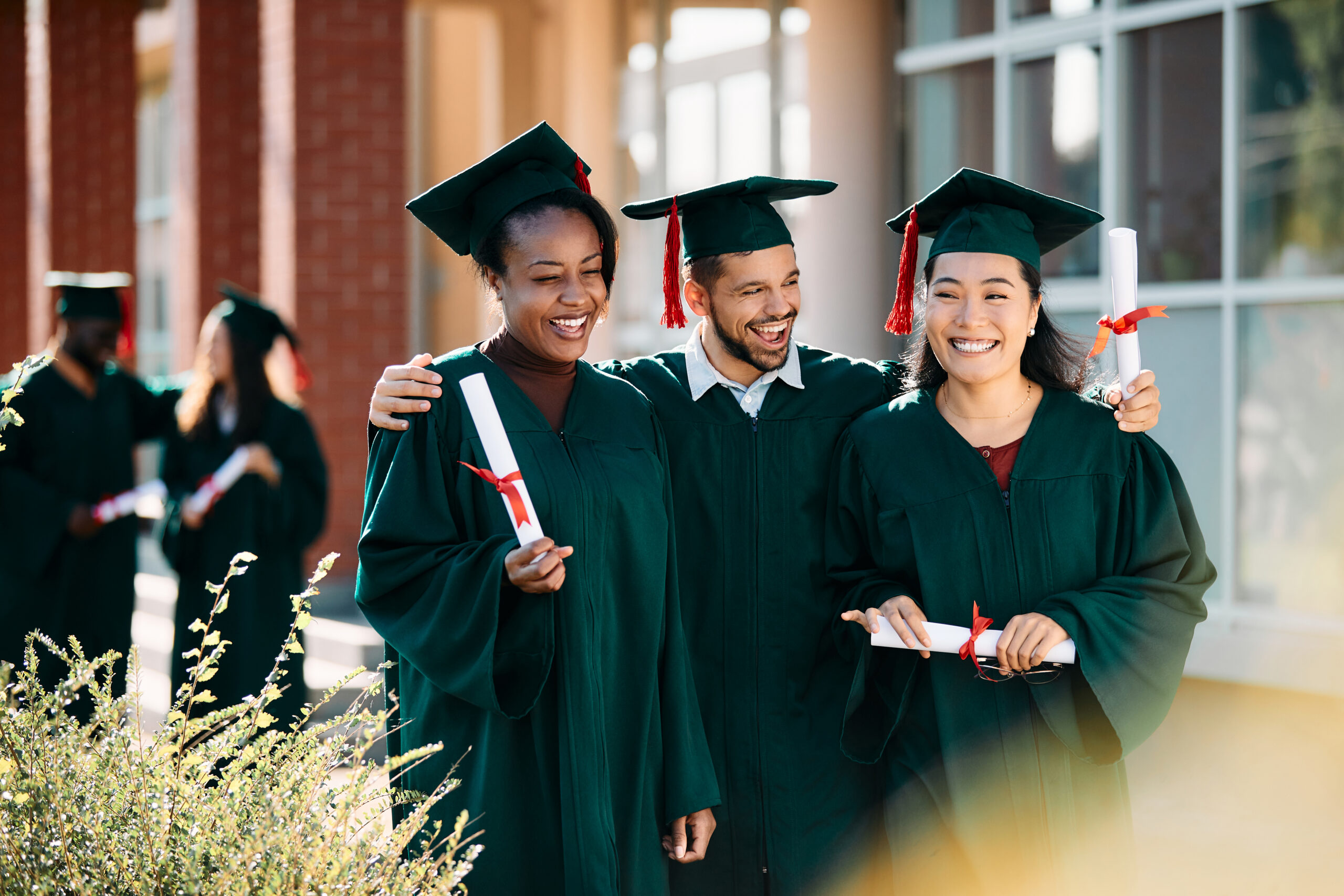 A group of graduates in dark green gowns and caps, happily celebrating their graduation day.